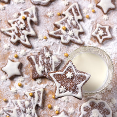 Christmas homemade chocolate cookies decorated with icing and powdered sugar with milk on a wooden background, top view