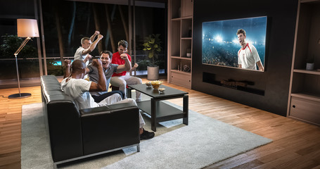 Group of students are watching a soccer moment on the TV and celebrating a goal, sitting on the couch in the living room.