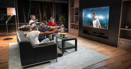Group of students are watching a soccer moment on the TV and celebrating a goal, sitting on the couch in the living room.