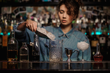 Female bartender adding to the measuring glass cup an ice cubes