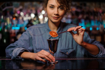 Smiling female bartender adding a dried tomato with tweezers to a cocktail glass with alcoholic drink