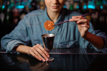 Female bartender adding a dried tomato with tweezers to a cocktail glass with alcoholic drink