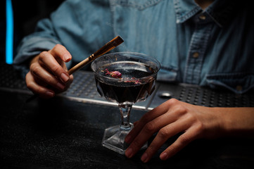 Bartender adding a glitter from the brush to a cocktail glass with alcoholic drink decorated with rose petals