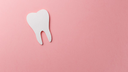 White tooth on pink background with copy space. Oral dental hygiene. Teeth whitening. Dental health concept. Oral care, teeth restoration. Dentist day concept. Flat lay. Top view. Pastel colors