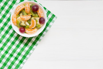 Bowl of healthy fresh fruit salad on white wooden background, top view, copy space