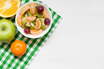 Bowl of healthy fresh fruit salad on white wooden background, top view, copy space