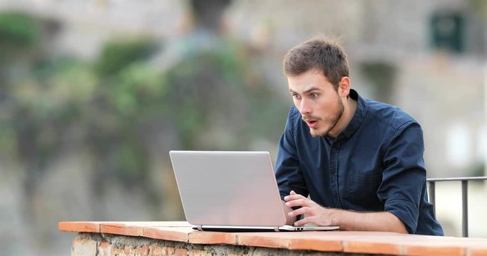 Surprised man finding content on a laptop in a rural apartment balcony
