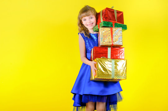 Festive Emotions, Beautiful Young Girl In A Festive Blue Dress Holding A Lot Of Gifts And Smiling, In The Studio On A Yellow Background