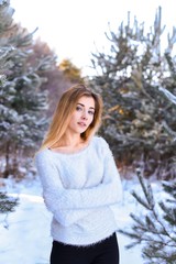 Outdoor waist up portrait. Young beautiful happy smiling girl walking on pine forest . Model with blue eyes,wearing stylish sweater. Magic snowfall. Space for text