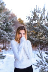 Outdoor waist up portrait. Young beautiful happy smiling girl walking on pine forest . Model with blue eyes,wearing stylish sweater. Magic snowfall. Space for text