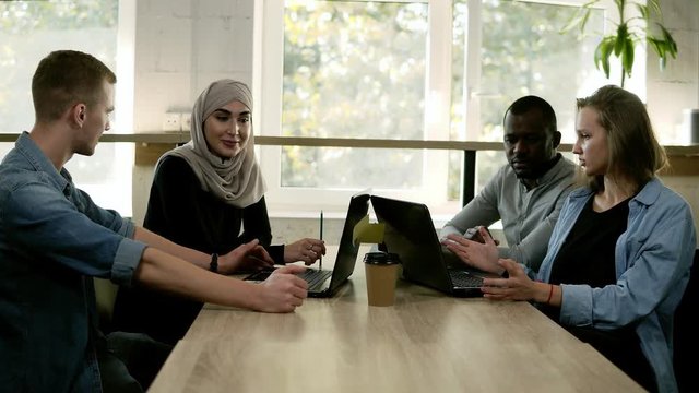 Diverse people using laptops while sitting at bright work place in front the window, multi-ethnic and multi cultural young people working as team, discussing start-up. Overview, accelerating footage