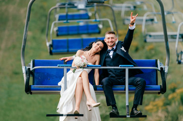 Happy wedding couple riding cableway from mountain in summer. Smiling cheerful bride in white...
