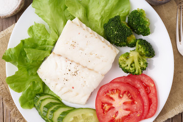 Steamed cod fish. Paleo, keto, fodmap healthy diet with vegetables on white plate on wooden table, top view.