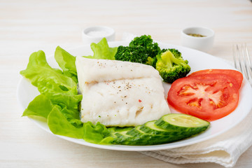 Fototapeta na wymiar Steamed cod fish. Paleo, keto, fodmap healthy diet with vegetables on white plate on white table, side view.