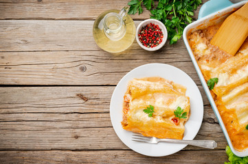 Cannelloni with filling of ground beef, tomatoes, baked with bechamel tomato sauce, top view, old dark wooden background, copy space