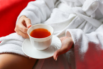 Portrait of the beautiful woman dressed in a bathrobe drinking tea in the morning in the hotel room. 