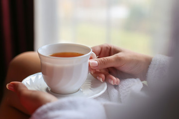 Portrait of the beautiful woman dressed in a bathrobe drinking tea in the morning in the hotel...