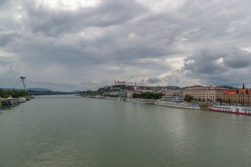 Panoramic view in a cloudy day of the Danube River with moored cruise ships, the Ufo(Most SNP) Bridge , Cathedral of Saint Martin and the Bratislava Castle in background.