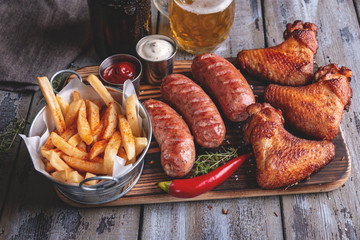 Grilled chicken wings,sausages french fries, white and red sauce on a wooden surface. 