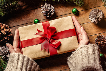 Female hands holding Christmas gift box on wooden table. Personal point of view