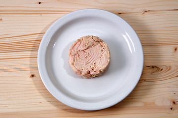 Looking down at Solid white albacore tuna fish on white plate still shaped like the can it came in on wooden table.