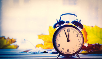 Retro alarm clock and maple leaves with rain drops on window. Autumn season image