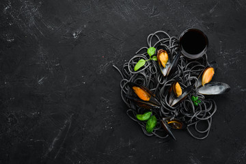 Black pasta with mussels on a black stone background. Top view. Free space for your text.