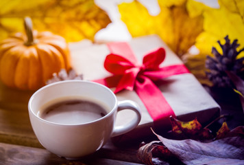 Gift box and maple leaves wih cup of coffee near window with rain drops.