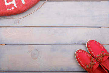 Red boat shoes on wooden background near lifebuoy and rope. Top view. Copy space