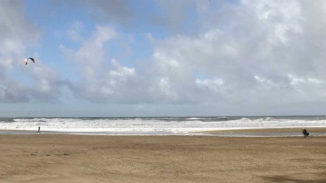 beach in front of the ocean with high waves, wind and a man doing kitesurfing on wheels on the beach