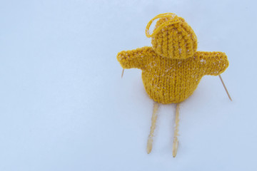 Knitted by hand on the needles little man, yellow color stands on skis in the snow. Winter day, close-up.
