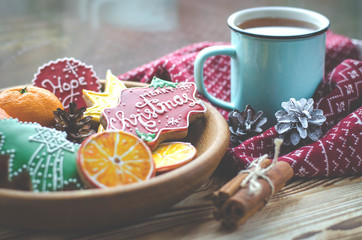 A cup of hot tea stands on a wooden table next to a wooden plate on which are gingerbread cookies made from orange slices against the background of a window with water drops