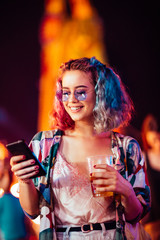 Young woman at the festival drinking beer and using mobile phone