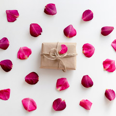 Gift in craft paper with pink rose petals background on white table. Romance concept. Flat lay, top view, copy space