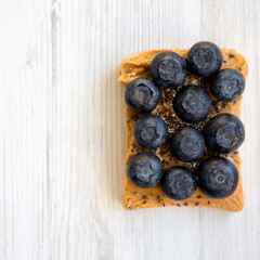 Toast with peanut butter, blueberries and chia seeds on a white wooden background, top view. Healthy dieting.