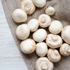 Fresh champignon mushrooms on cloth. White wooden background. Top view, from above, overhead.