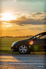 beautiful black modern car stands on asphalt road in summer illuminated by the rays of the sunset