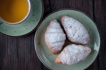 Freshly baked croissants cup with green tea on a brown wooden background.