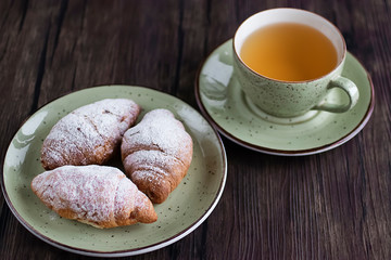 Freshly baked croissants cup with green tea on a brown wooden background.