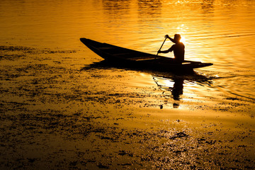 Silhouette of a man peddling in a boat at sunset