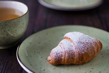 Freshly baked croissants cup with green tea on a brown wooden background.