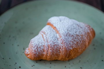 Freshly baked croissants cup with green tea on a brown wooden background.