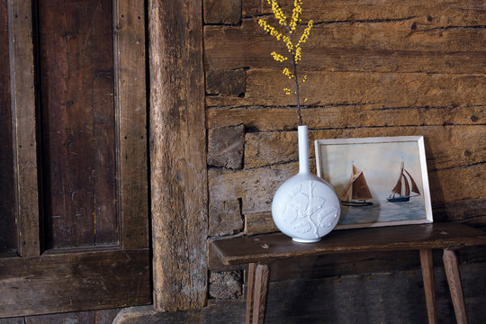 Blume in weisser Porzellan Vase vor Bild mit Segelbooten und alter Holzwand