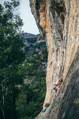 woman climbs a rock in Greece and beautiful forest and cliff landscape on the background