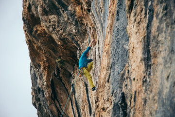 man in yellow pants and blue t-shirt climbs a rock top rope