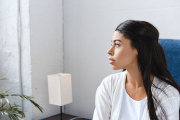 beautiful mixed race girl in white robe sitting on bed and looking away in morning - Powered by Adobe