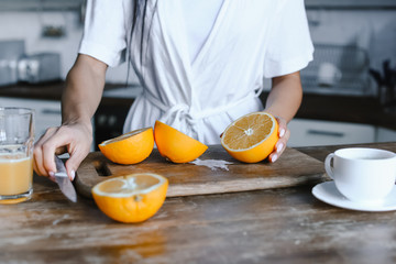 cropped image of mixed race girl in white robe preparing orange juice in morning and cutting oranges in kitchen - Powered by Adobe
