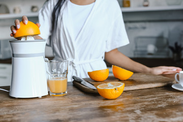 cropped image of mixed race girl in white robe preparing orange juice in morning in kitchen - Powered by Adobe
