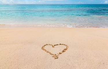 A heart drawn in the white sand of a Caribbean beach, with turquoise blue ocean in the background.