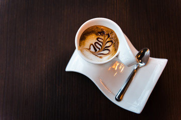 Beautiful cup of cappuccino coffee with plate on dark wooden table